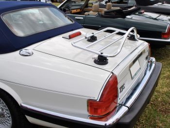 white jaguar xjs convertible with a blue hood at a car show with a stainless steel luggage rack attached to the boot
