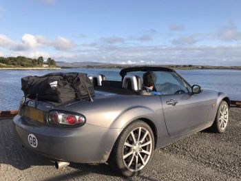 grey mazda mx5 mk3 miata nc soft top with a boot-bag vacation luggage rack fitted next to the sea